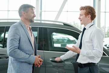 Poster - Young confident sales manager consulting mature male customer in auto center