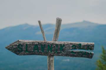 Wooden signboard with writing Slavnik, the name of the hill in Slovenian coastline, with the same hill being visible in the background.