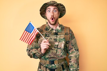 Canvas Print - Young caucasian man wearing camouflage army uniform holding usa flag scared and amazed with open mouth for surprise, disbelief face