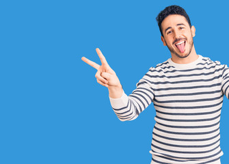 Young hispanic man wearing casual clothes smiling with tongue out showing fingers of both hands doing victory sign. number two.