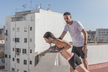 Young Female Athlete Doing Incline Push-ups On The Roof Of A Building, While Being Supervised By Her Personal Trainer