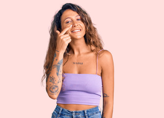 Young hispanic woman with tattoo wearing casual clothes pointing with hand finger to face and nose, smiling cheerful. beauty concept