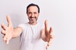 Middle age handsome man wearing casual t-shirt standing over isolated white background looking at the camera smiling with open arms for hug. Cheerful expression embracing happiness.