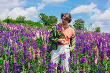 Tall handsome man standing on lupine flowers field holding lupine flowers in hand