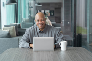 Wall Mural - Smiling business senior old elderly Black American man, African person working from home on table with computer notebook laptop in quarantine in corona virus pandemic concept.