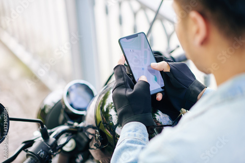 Fotomural Motorcyclist in fingerless gloves checking map on smartphone screen before ridin