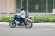 © DragonImages - Young man in helmet with backpack riding fast on motorcycle along city roads