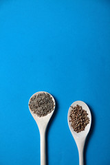 two wooden spoons of coriander and cumin on blue background flat lay. Image contains copy space