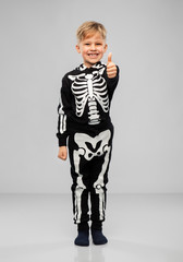 Wall Mural - halloween, holiday and childhood concept - smiling boy in black costume with skeleton bones showing thumbs up over grey background