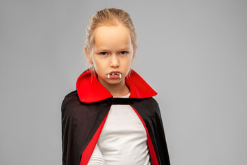 halloween, holiday and childhood concept - girl in black dracula costume with cape and fangs over grey background