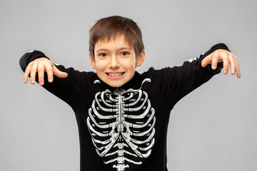 Wall Mural - halloween, holiday and childhood concept - boy in black costume of skeleton frightening over grey background