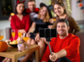 Sticker - friendship, holiday and people concept - group of happy smiling friends in halloween costumes taking picture with smartphone on selfie stick at home party at night