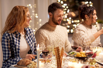 Wall Mural - holidays, celebration and people concept - happy smiling friends having christmas dinner party at home in evening