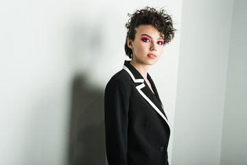 A young girl with a strange hairstyle and pink make-up on a white background in a black suit