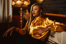 African American Fashionable Woman With Many Braids Hairstyle, Wearing Stylish Yellow Blouse, Posing In Dark Vintage Luxury Interior. Copy, Empty Space For Text
