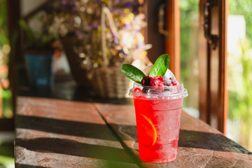 Cold raspberry juice with ice and leaf wooden top.