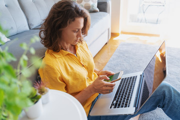 Wall Mural - A beautiful young femal in a yellow shirt sits on the floor on a carpet with a laptop, freelancer and home office concept. Work from home