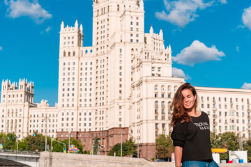 Wall Mural - A young woman in a black jacket with an inscription walks along the embankment with a view of the Moscow river and the Stalin high-rise in Moscow