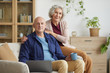 © Seventyfour - Portrait of happy senior couple smiling at camera while posing sitting on couch in cozy home interior, copy space