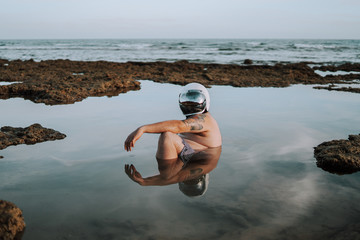 Wall Mural - Selective focus shot of a middle aged man with a helmet swimming in a small rocky lake
