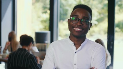 Wall Mural - Portrait of happy young successful African businessman smiling at camera, looking serious at modern office slow motion.