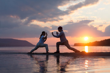 Man and woman doing Tai Chi chuan at sunset on the beach.  solo outdoor activities. Social Distancing. Healthy lifestyle  concept. 