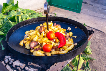 Fried potatoes with pork and mushrooms, garnished with tomatoes and chili in a pan