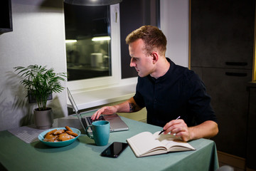 A freelancer works from home in the kitchen and using a laptop. Successful man working with a laptop and reading good news. Handsome successful entrepreneur sits and works in his modern home.