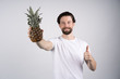 © Ivan - Man with long beard holds pineapple in hands. Dieting and fitness. Look at camera and shows thumb up
