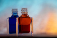 Two Bottles Of Aurasoma With A Red And Bluu Essence Against An Abstract Background.