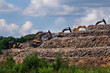 Garbage landfill in the Moscow region. Excavators level the garbage pile at the trash dump. Summer sunny day. Bushes and trees grow around the dump, the grass is green. Blue sky with some clouds.