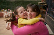 © Cavan Images - Side view of cheerful woman hugging daughter while resting on bench