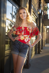 Poster - Beautiful smiling blonde female with curly hair wearing a red off shoulder blouse and shorts