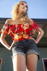 Sticker - Beautiful blonde female with curly hair wearing a red off shoulder blouse and shorts