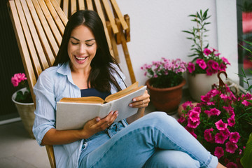 Young beautiful happy woman relaxing on cozy balcony, reading a book,