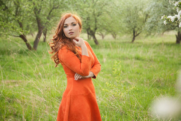 Portrait of a red-haired girl walking in an apple orchard in an orange dress