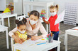 © ShunTerra - A teacher helps a schoolgirl with a mask on her face draw in a copybook at school during a lesson after being quarantined and blocked by covid19.