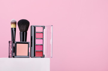 Set of cosmetic products lipsticks, powder, makeup brushes on pink background. Beauty products for professional fashionable makeup by a make-up artist. Women's accessories for skin care. Copy space