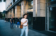 © BullRun - Stylish young woman using cellphone while walking on city street