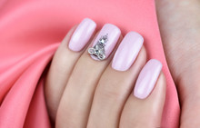 Women's fingers with soft pink manicure and rhinestones on the nails. Pink background.