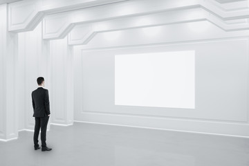 Sticker - Businessman standing in white classical interior with blank billboard on wall.