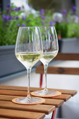 Close up of two glasses of white wine standing on a wooden table, flower pot in background