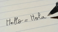 Beginner Spanish language learner writing Hello word Hola for homework on a notebook