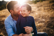 Father Holding Son Smiling In A Field With Golden Light