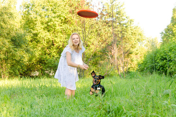 Wall Mural - A beautiful blonde young woman throws a frisbee after which a dog runs