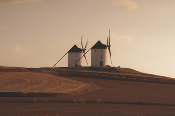 Dos viejos molinos de viento situados en lo alto de una colina miran hacia Campo de Criptana (Ciudad Real) en el atardecer. Molinos con los que soñaba Don Quijote de La Mancha.