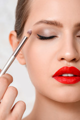 Wall Mural - Makeup artist working with model on light background, closeup