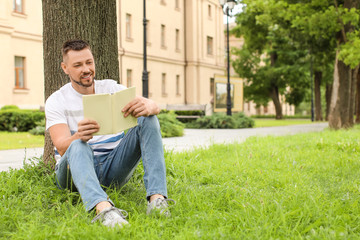 Sticker - Handsome man reading book while relaxing in park