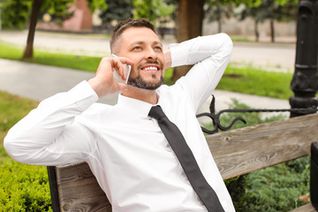 Wall Mural - Handsome businessman talking by phone while relaxing in park