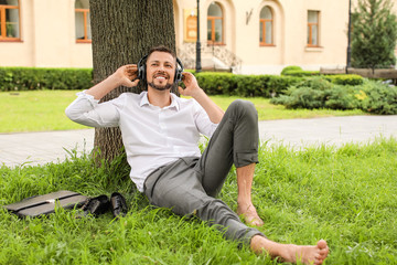 Wall Mural - Handsome businessman listening to music while relaxing in park